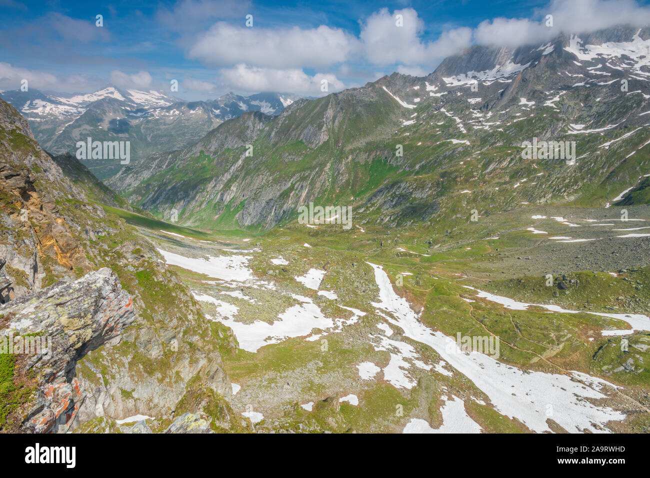 Snow patches on the slopes of the Alps between the Italian and Austrian border. Lingering snow on the mountains, zig-zagging trail dropping below. Stock Photo