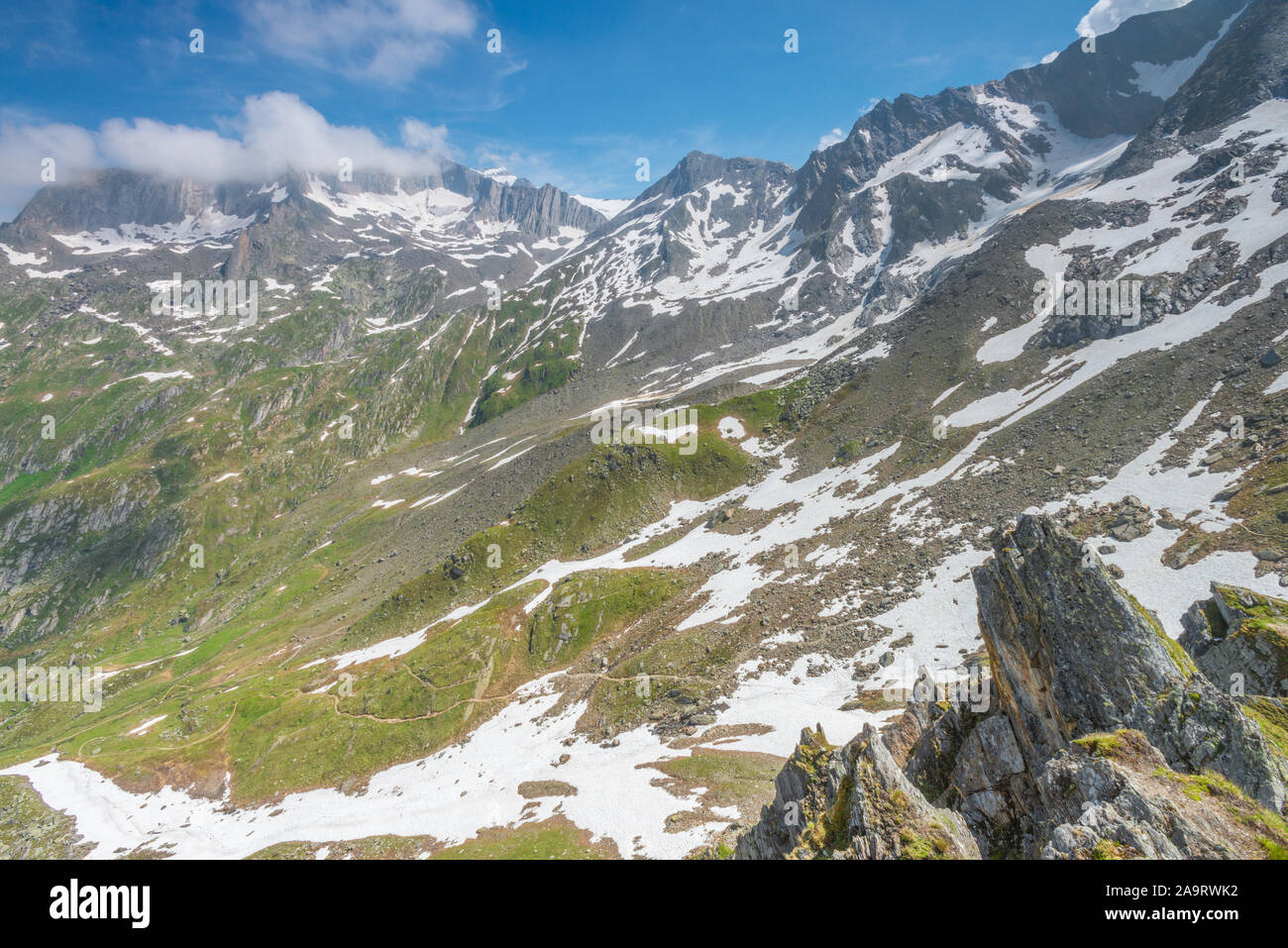 Snow patches on the slopes of the Alps between the Italian and Austrian border. Lingering snow on the mountains, zig-zagging trail dropping below. Stock Photo