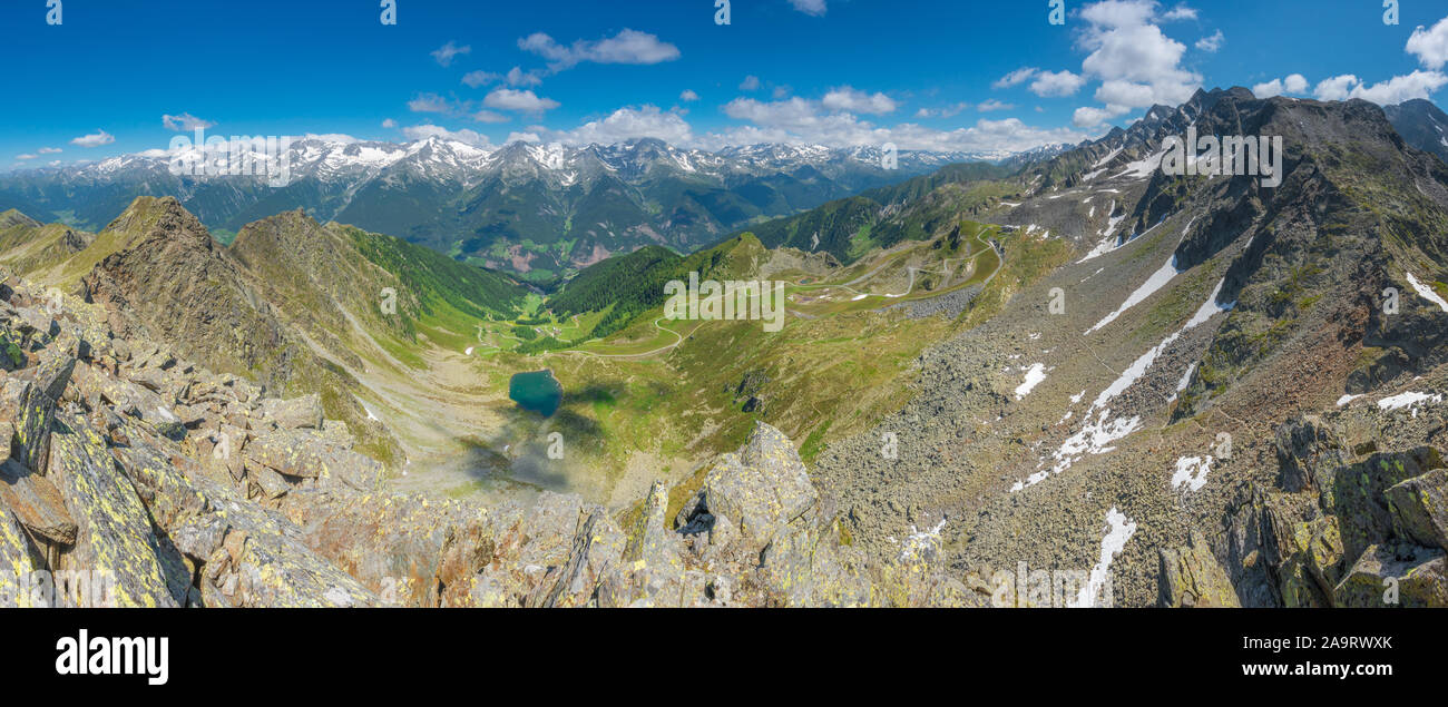 Panoramic view from the summit, open views of Valle Aurina - Ahrntal. Blue alpine lake surrounded by rugged mountains. Snowcapped peaks of the Alps. Stock Photo