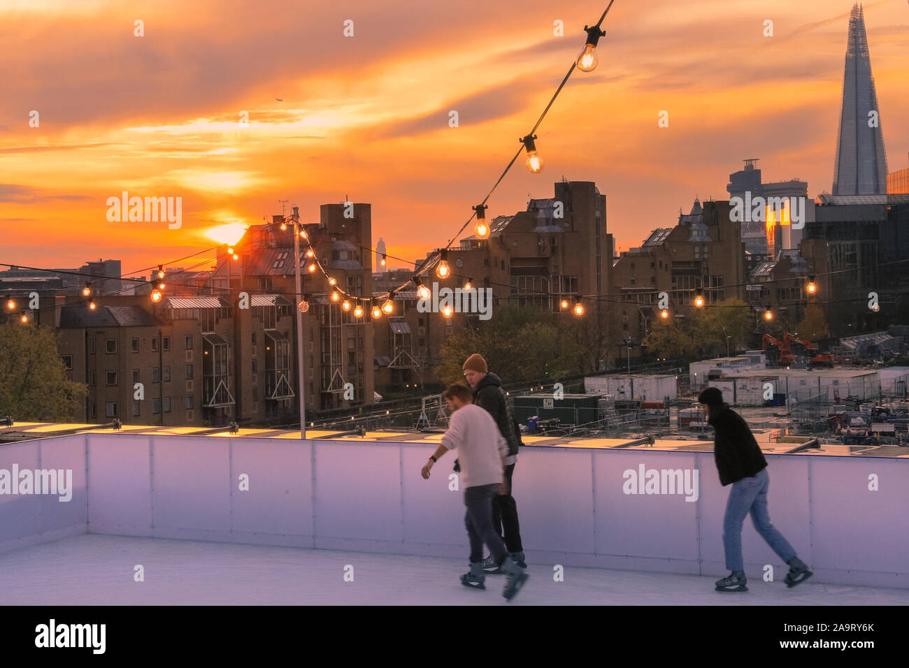 Tobacco Dock, London, UK, 17th November 2019. Skating at sunset. People enjoy spectacular views across to the City of London at London's trendy Skylight ice rink, a rooftop at the historic Tobacco Dock complex in Wapping, East London. Credit: Imageplotter/Alamy Live News Stock Photo