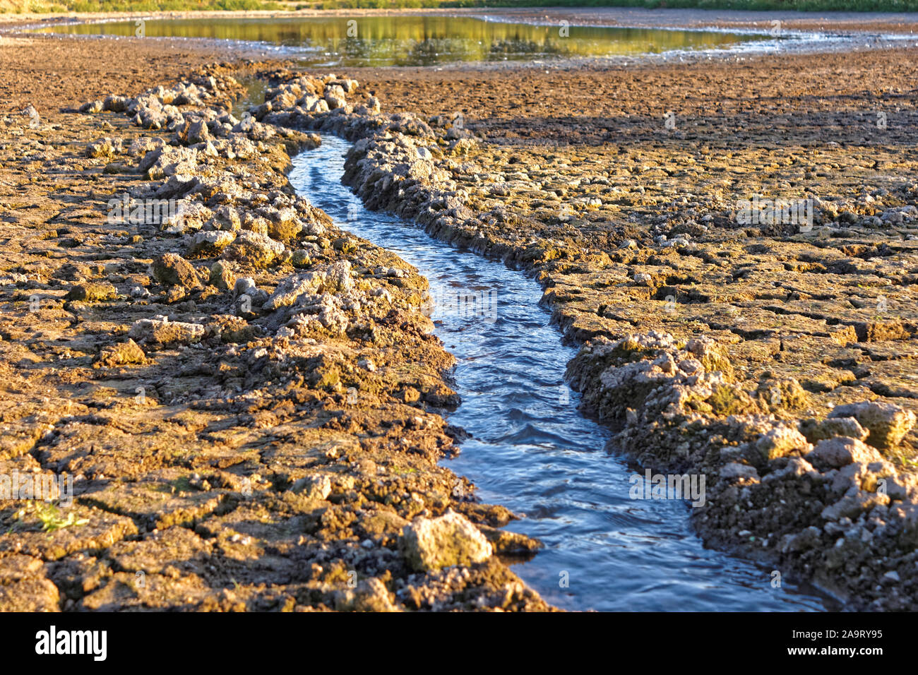 Water stream in artificially dug canal flows into the pond shrinking in