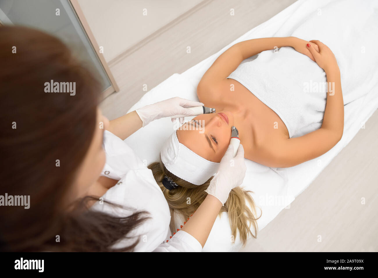 woman close up receiving electric facial massage on microdermabrasion equipment at beauty salon. rf lifting procedure in a beauty parlour. Top view Stock Photo