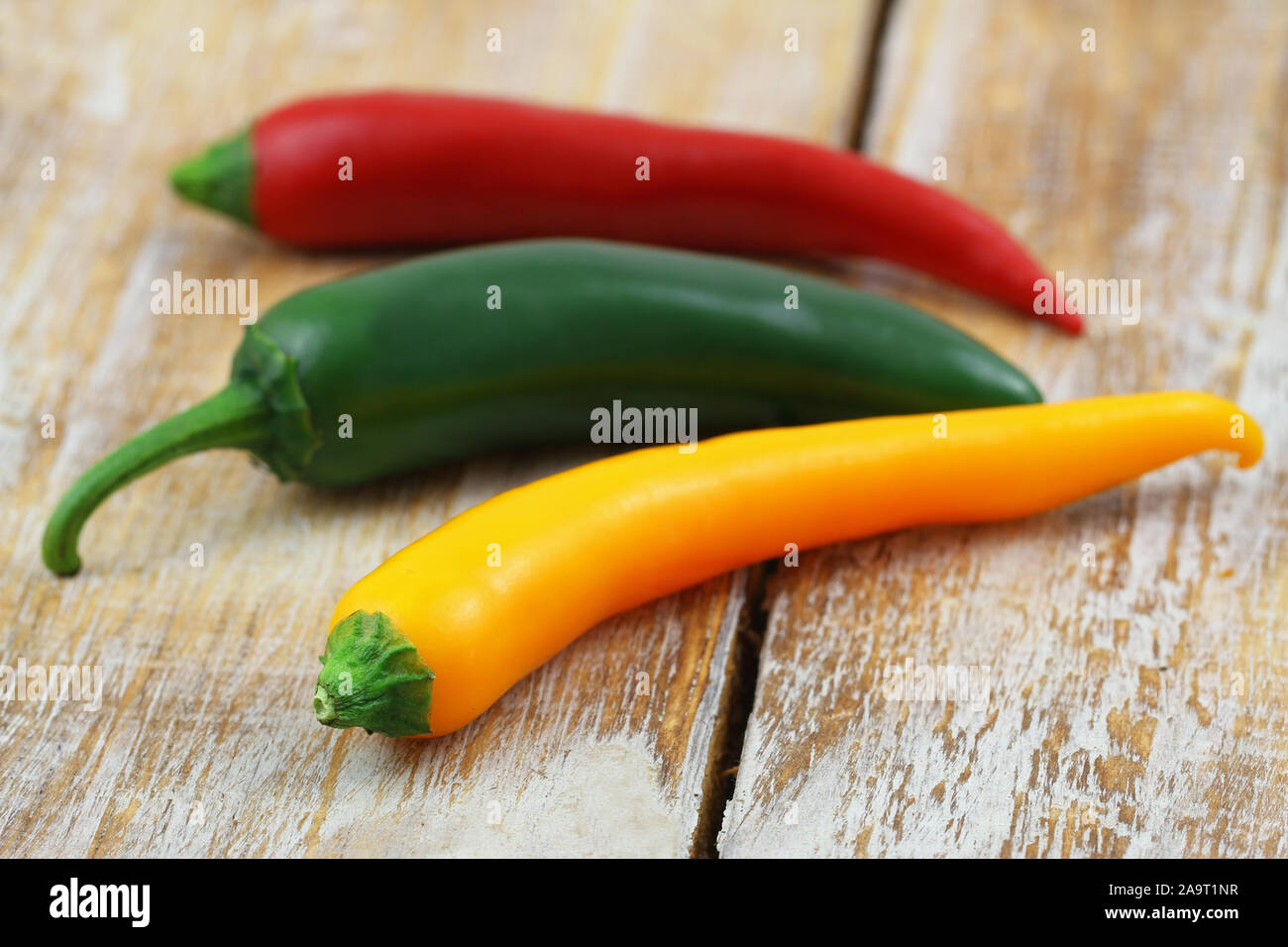Yellow, red and green chilli peppers on rustic wooden surface Stock Photo