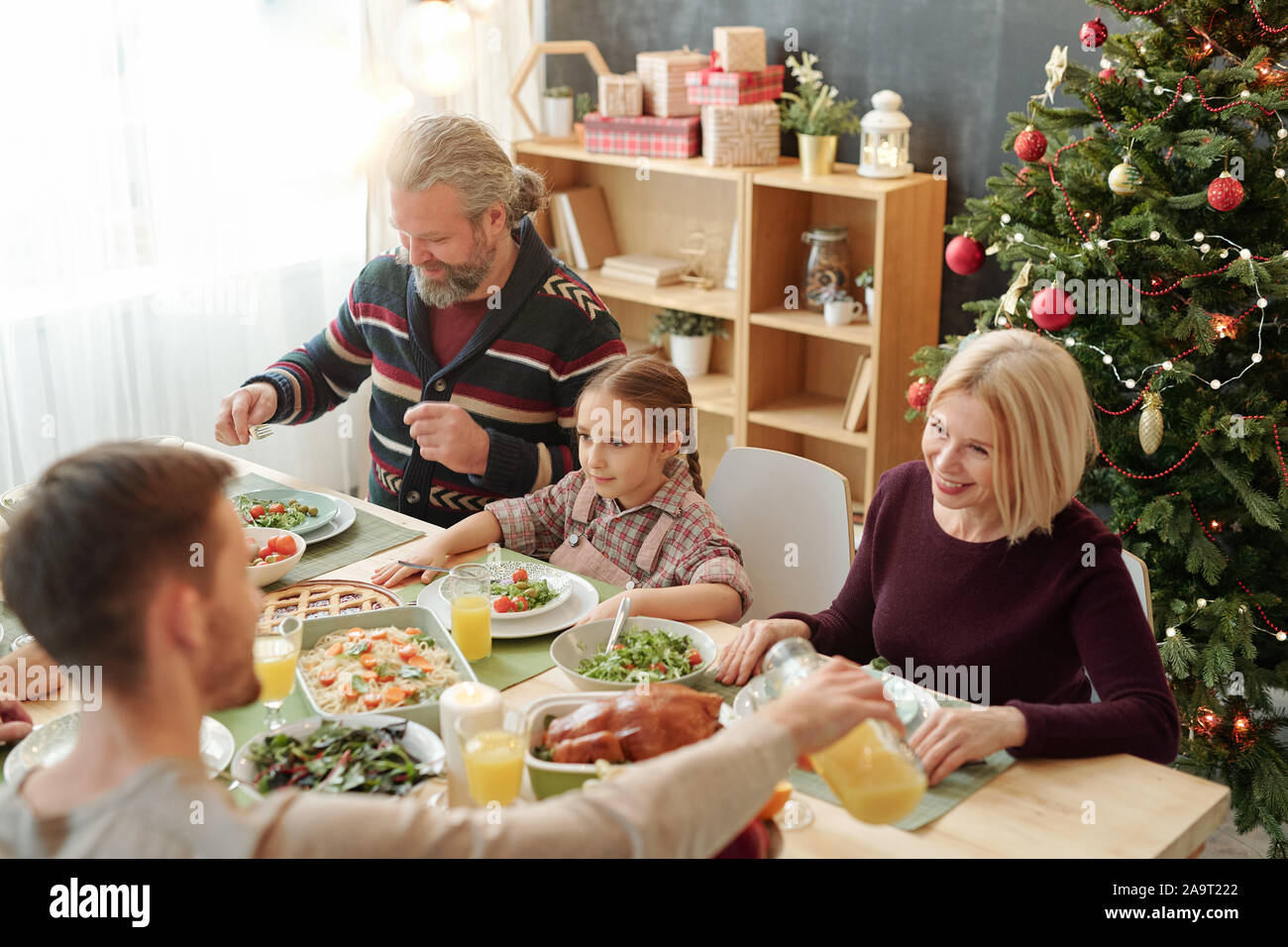 Young man pouring orange juice for mom sitting against decorated Christmas tree Stock Photo