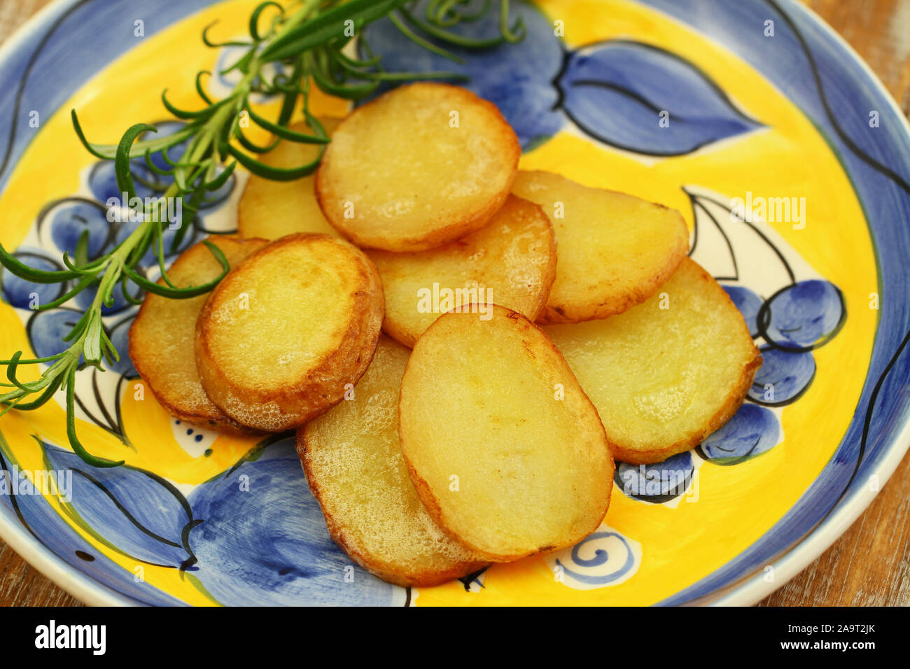 Slices of fried potatoes with fresh rosemary on vintage plate Stock Photo
