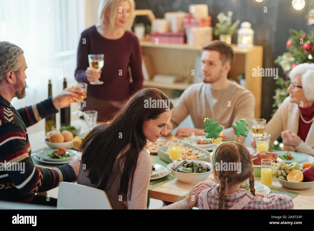Young mother and her little daughter sitting close to each other by served table Stock Photo