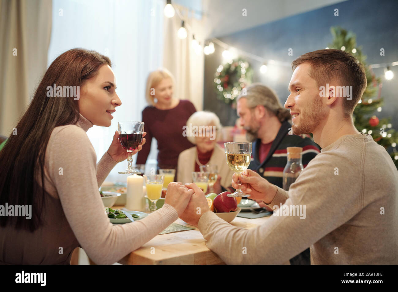 Young affectionate couple with glasses of wine making toast by served table Stock Photo