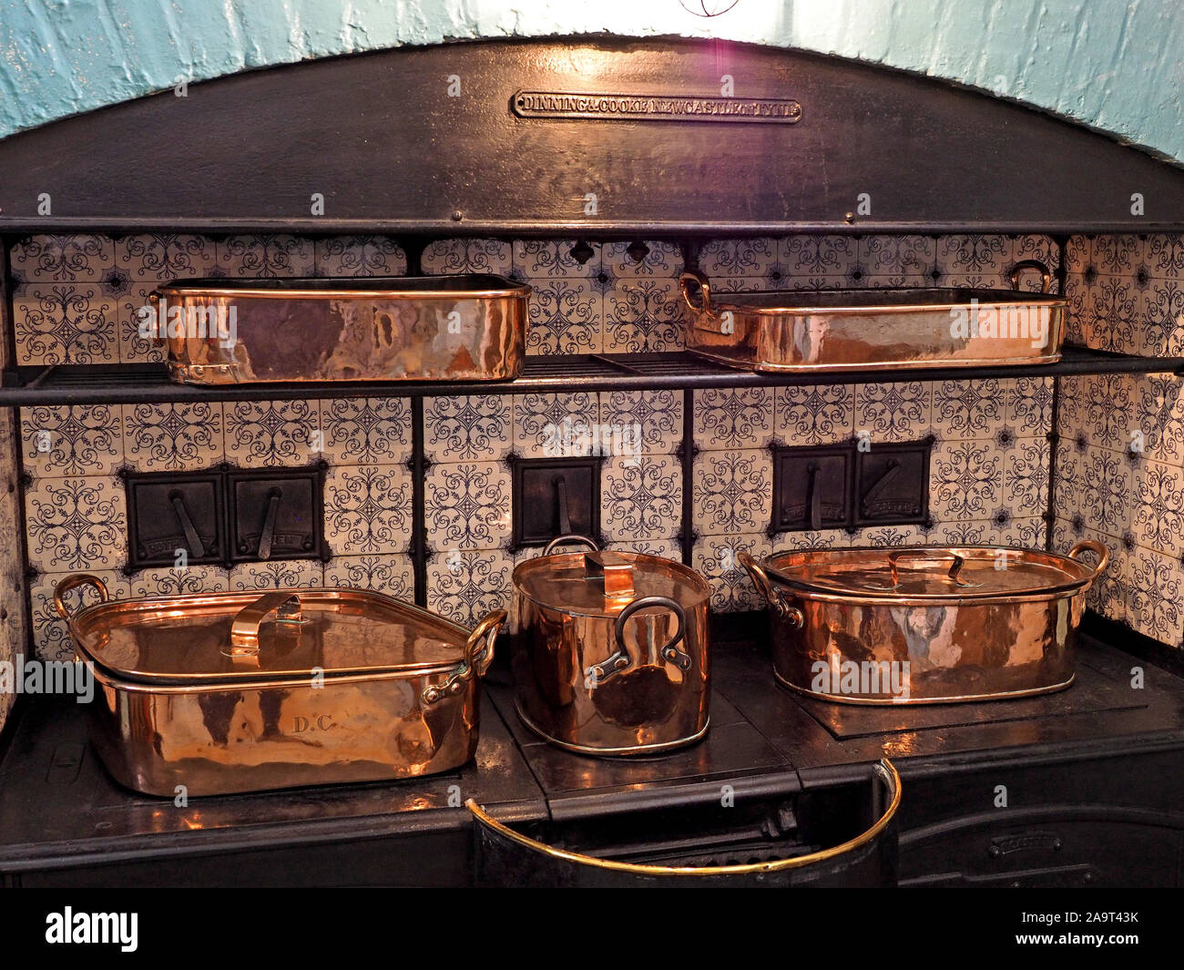 vast gleaming copper pans with lids forming part of historic display on cast iron  cooking range in kitchen of medieval castle in England, UK Stock Photo