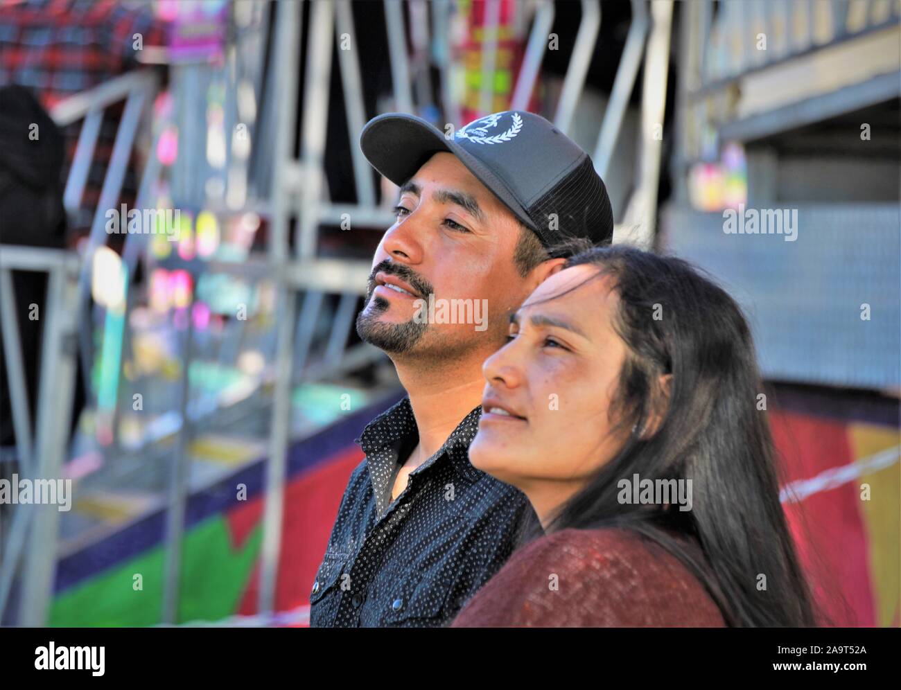 20s 30s Hispanic couple watching their kids have fun at a fair during the hot summer of CA USA Stock Photo