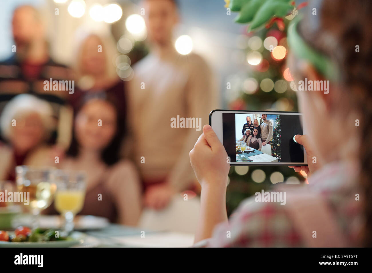 Little girl with smartphone taking photo of big happy family gathered for dinner Stock Photo