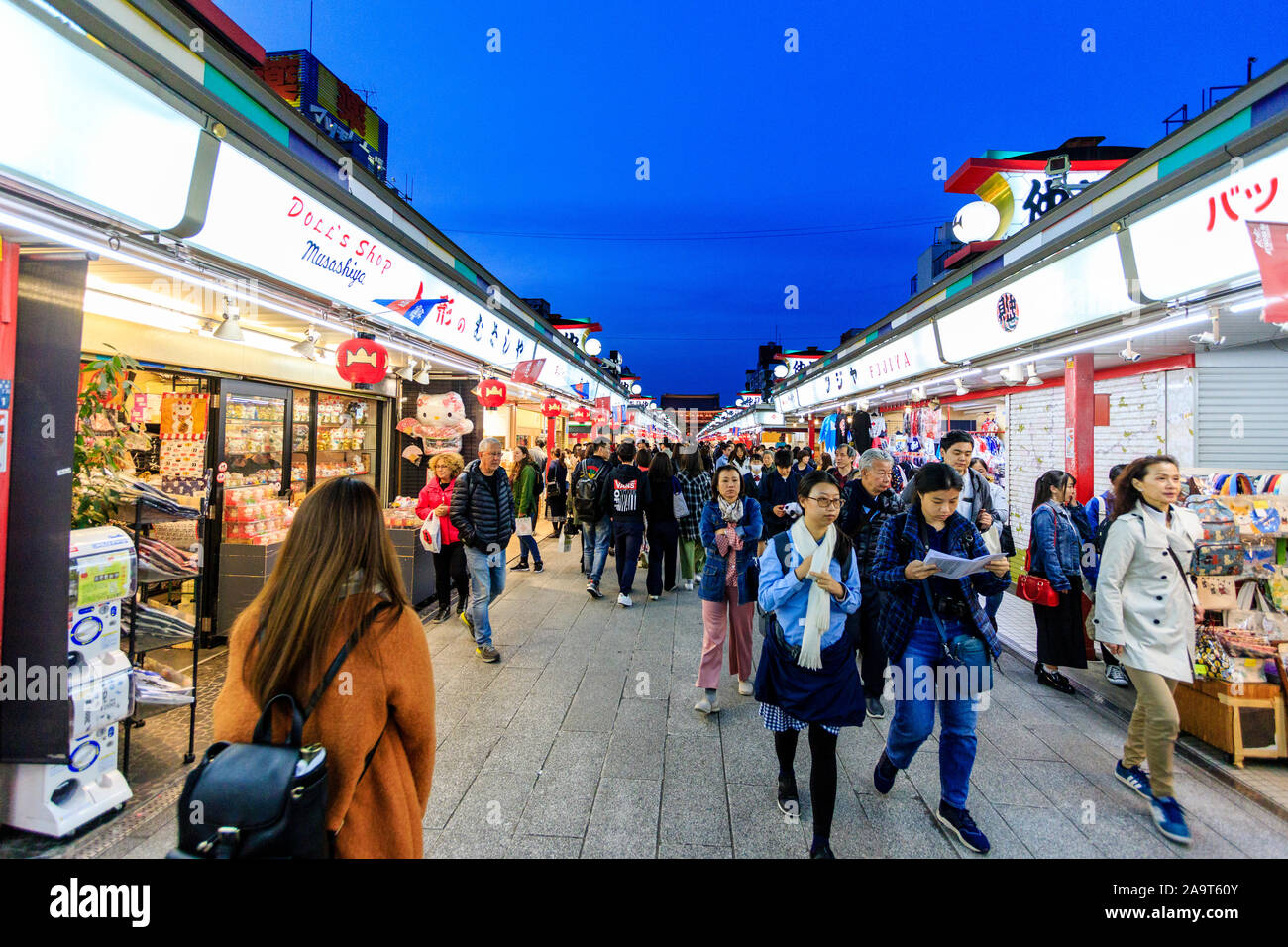 Tokyo, Asakusa shrine and Sensoji temple. Nakamise shopping street with people walking past food and souvenir shops with temple gate behind. Night. Stock Photo