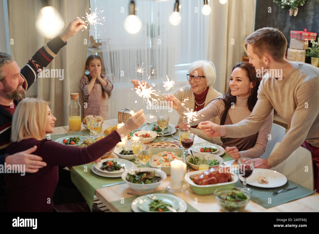 Happy young and mature adults with bengal lights sitting by served table Stock Photo