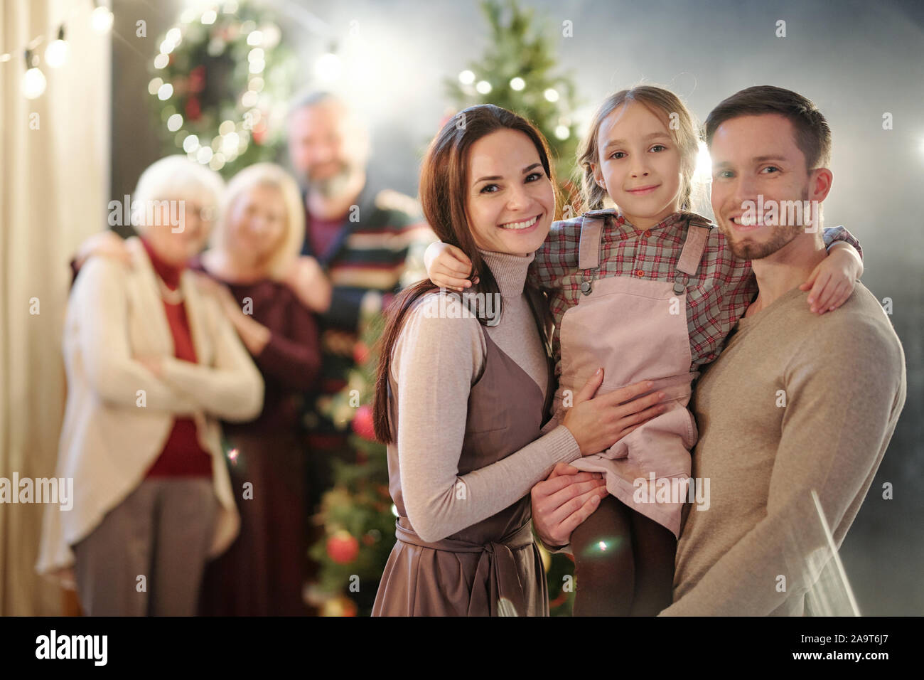 Happy young family standing in front of camera on background of mature adults Stock Photo