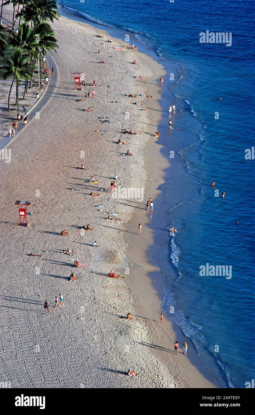 The crowds of sunbathers thin out as the sun sets on the white sands of famous Waikiki Beach, a popular destination for vacationers who come to the capital city of Honolulu on Oahu, one of the eight major islands in the Pacific Ocean that are part of the tropical state of Hawaii, USA. This aerial photograph shows only a small part of Waikiki Beach, which is two miles (3.2 kilometers) long and actually has eight sections with individual beach names. Most populated are the sands and walking promenades in front of historic and high-rise hotels along the meandering shoreline. Stock Photo