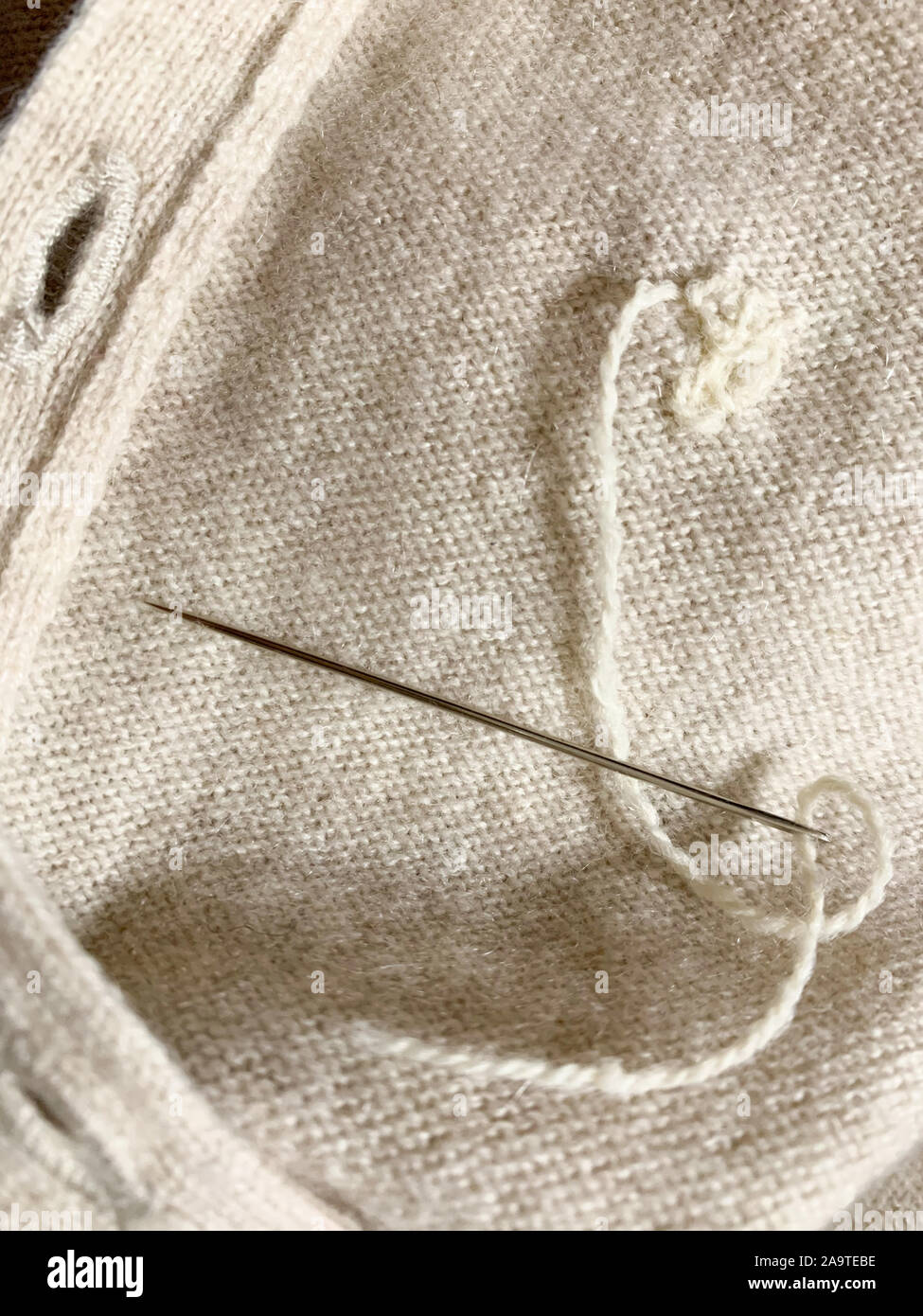 Expensive cashmere sweater with holes caused by cloth moths (Tineola bisselliella) is being repaired with a needle. Selective focus Stock Photo