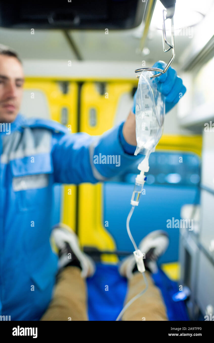 Gloved paramedic putting dropper on holder over sick person in ambulance car Stock Photo