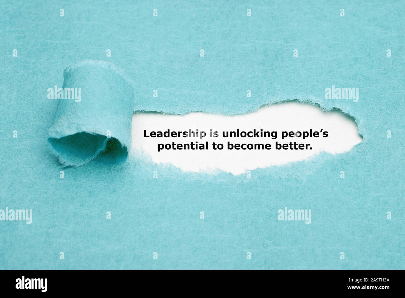Motivational quote 'Leadership is unlocking people’s potential to become better' appearing behind torn blue paper. Stock Photo