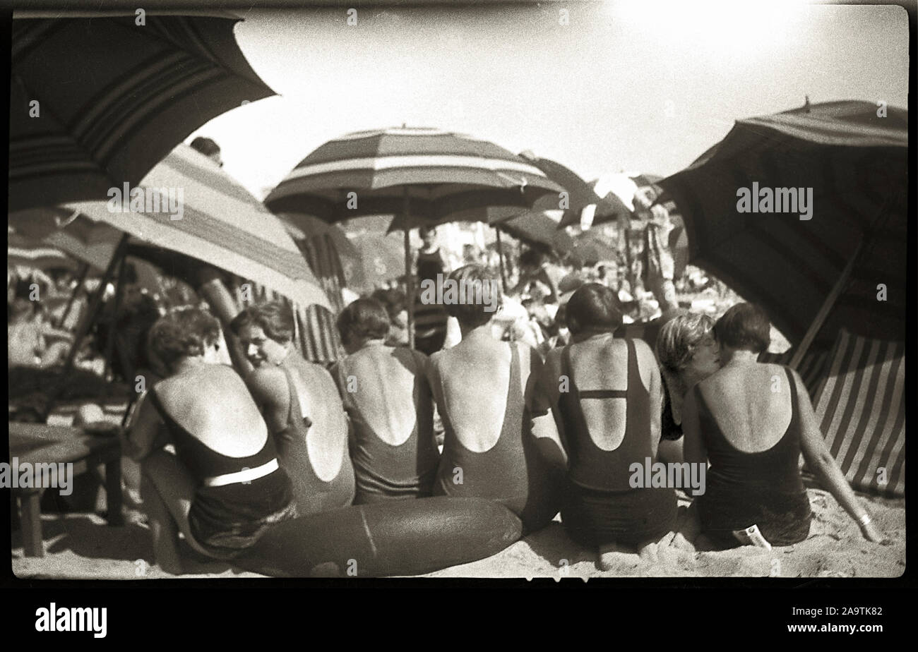 Bareback beach goers in the latest fashion sitting undwe umbrellas
