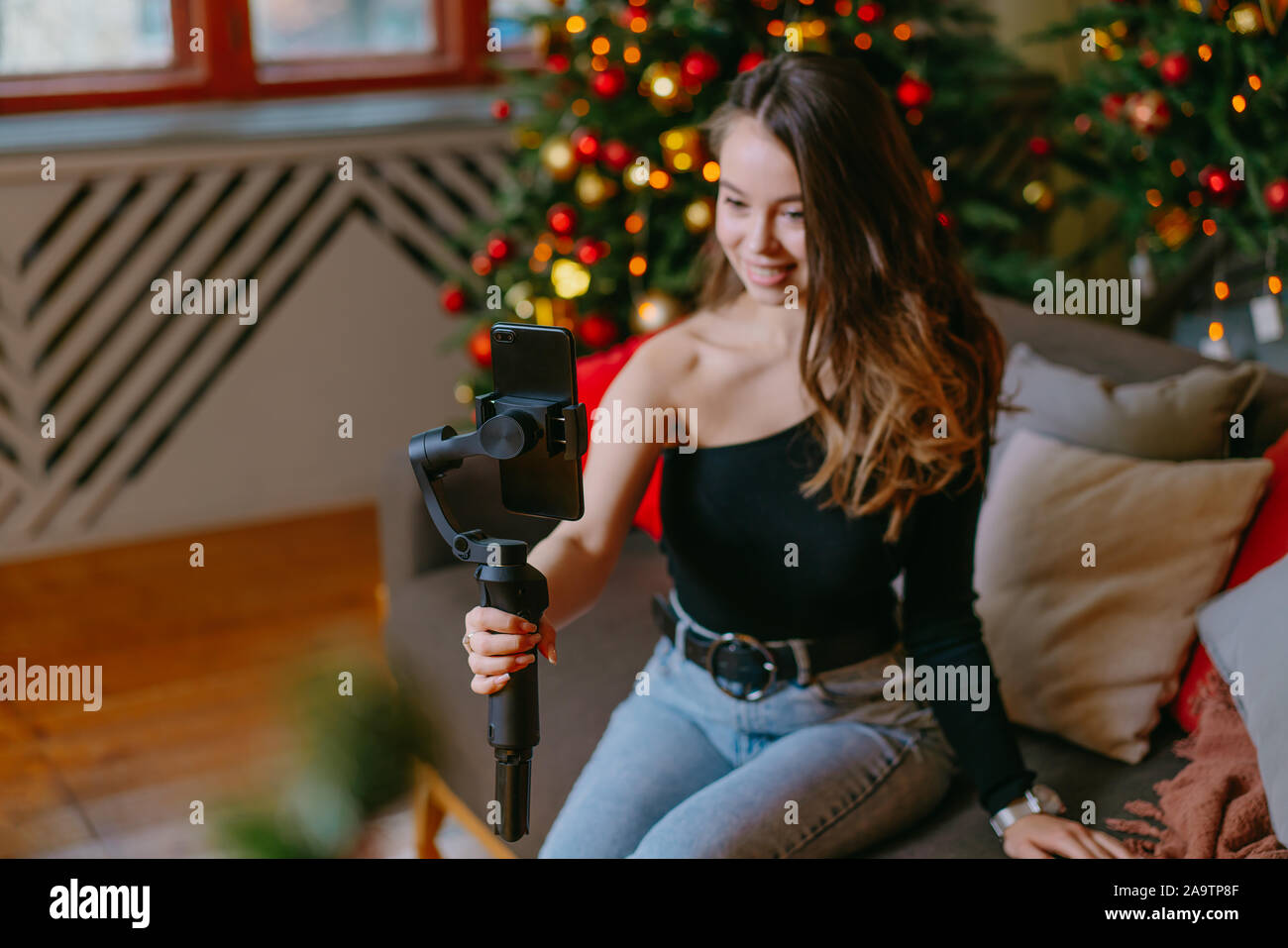 Young woman blogger is broadcasting on the phone with a stabilizer. Christmas and New Year. Side hustle. Indoor Stock Photo