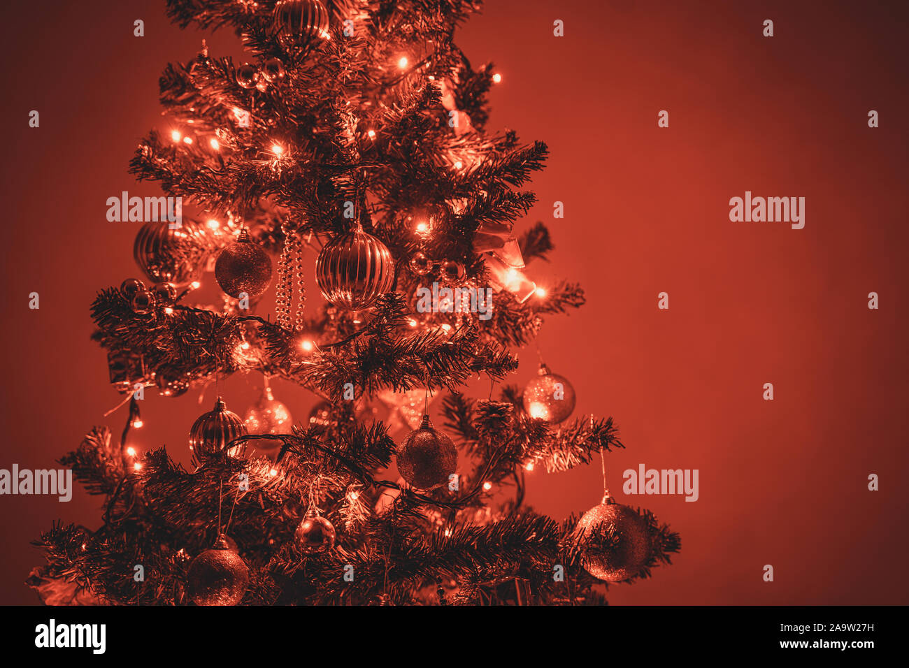 Photo of a christmas tree with red christmas lights and christmas ornaments. Space for copy or text on the right side of the picture. Stock Photo