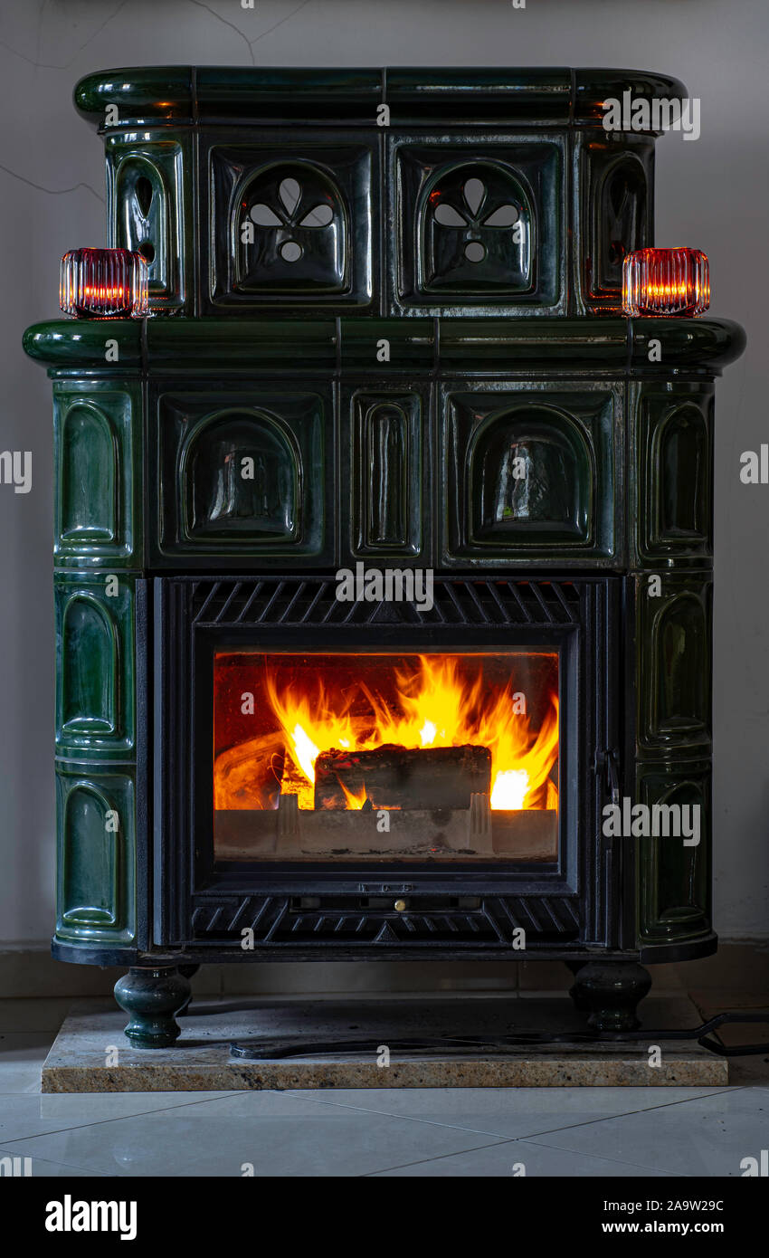 Green antique tile stove. Fire burning in the fireplace. Candles on a tile stove. Stock Photo