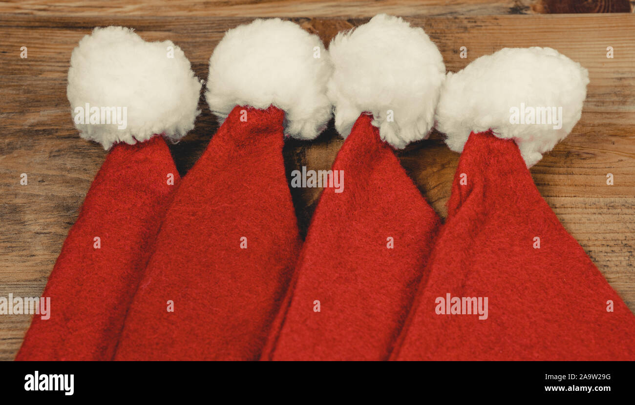 Christmas hats on a wooden table. 4 red santa hat on a vintage wood surface. Christmas concept. Santa Claus cap. Stock Photo