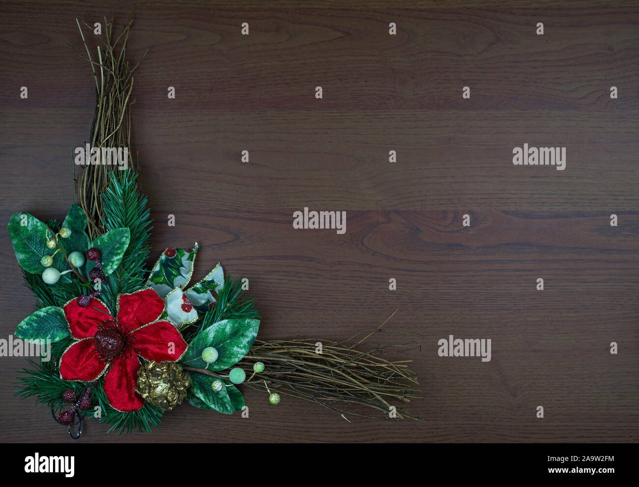 Christmas wreath isolated on wooden background. Big red flower and green leaves and twigs. Space for text or copy. Christmas or New Year. Stock Photo