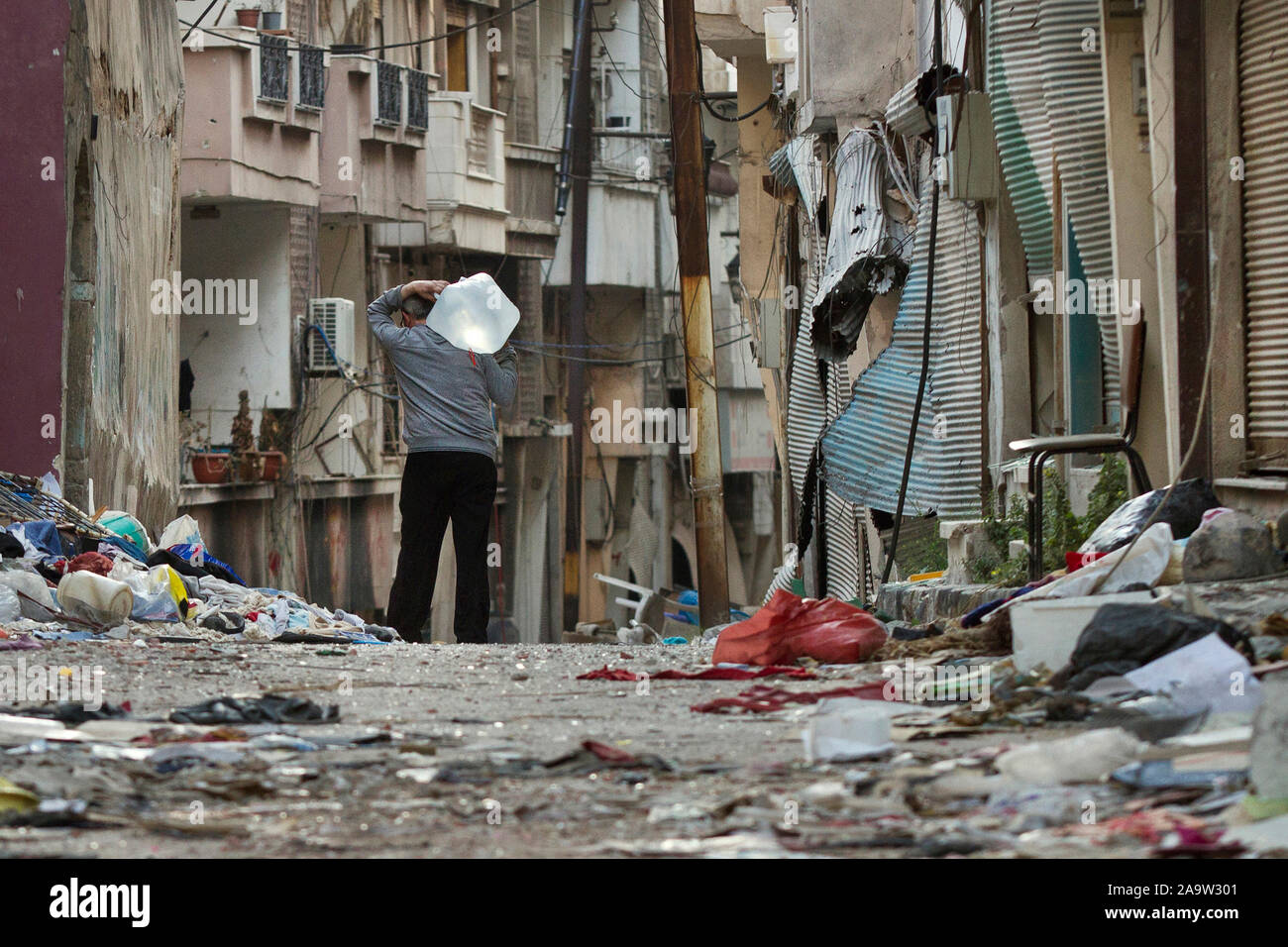 In a released neighborhood in the city of Homs, a recently returned resident carries a plastic tank of water to his home. Tanks containing drinking water by the aid stations have been located in the various locations. on 2014/May/19 Stock Photo