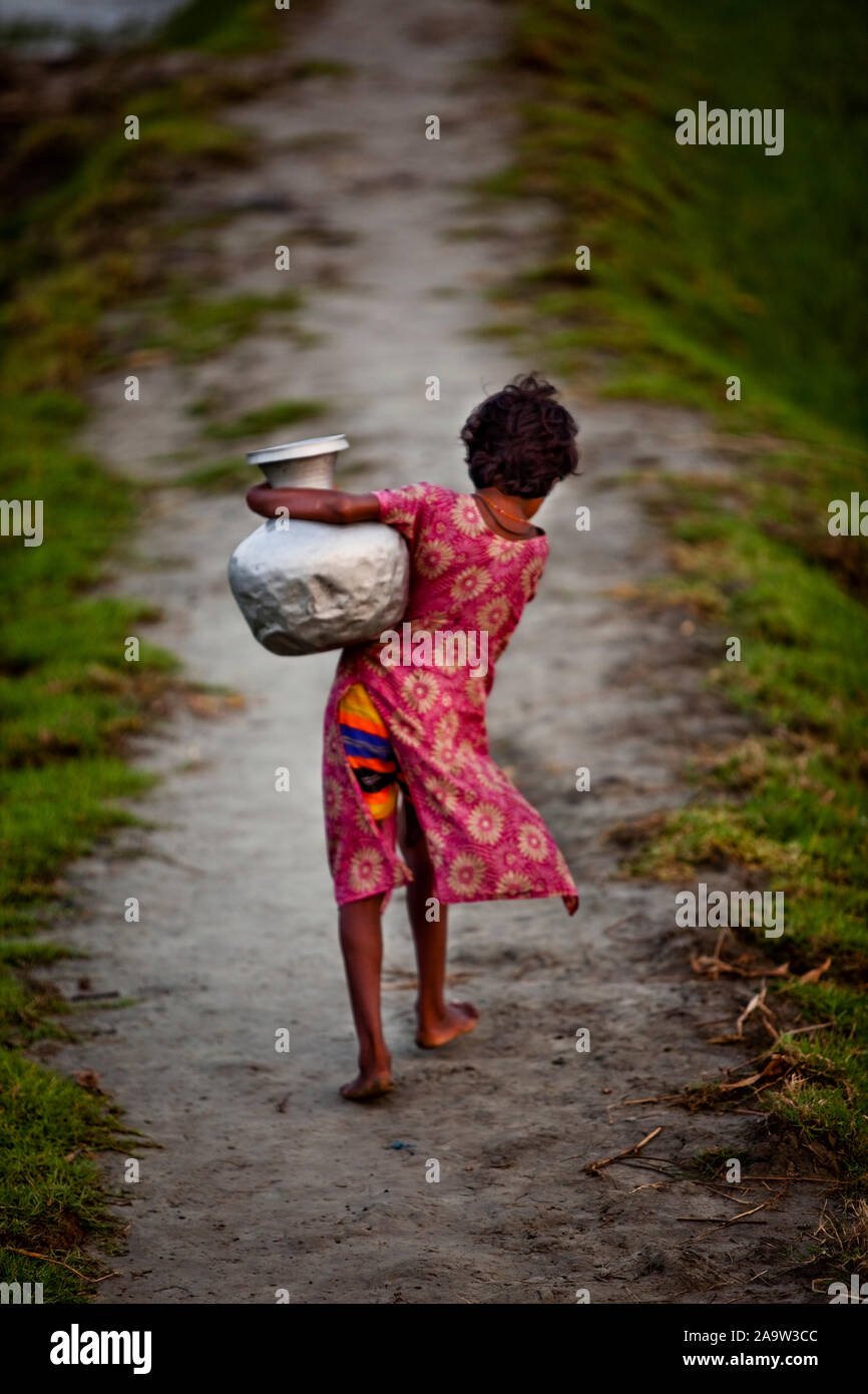 Drinking water is scarce in Nijhum Dweep, the Island of Silence. A girl carries drinking water from a far away tube well early in the morning Stock Photo