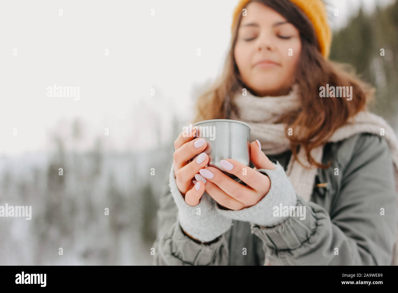 https://c8.alamy.com/comp/2A9WE89/brunette-girl-in-yellow-knitted-hat-with-metal-mug-of-hot-tea-in-the-forest-outdoors-in-winter-2A9WE89.jpg
