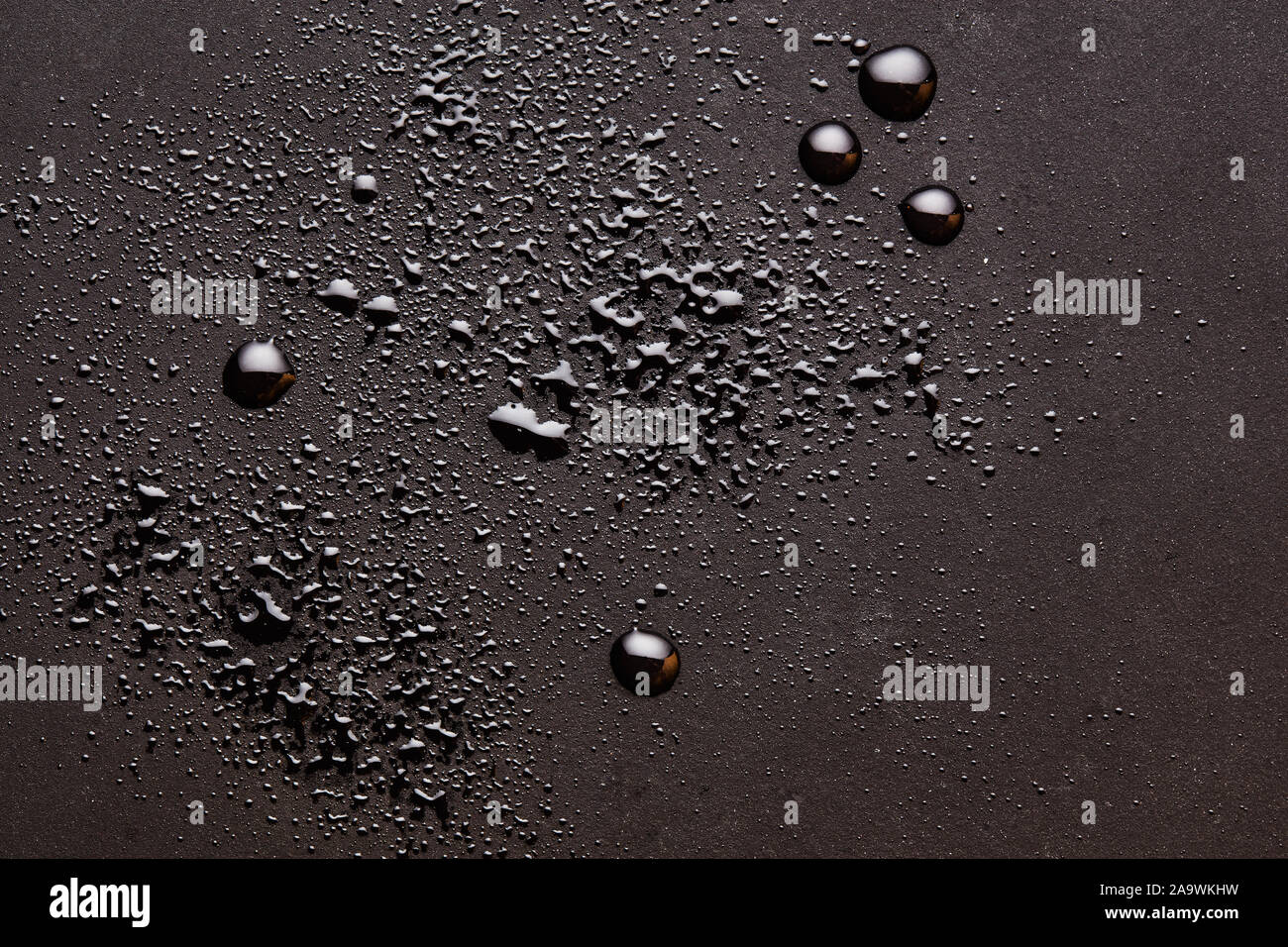 Shiny water drops on a dark brown moody surface. Abstract background with close up overhead view. Stock Photo