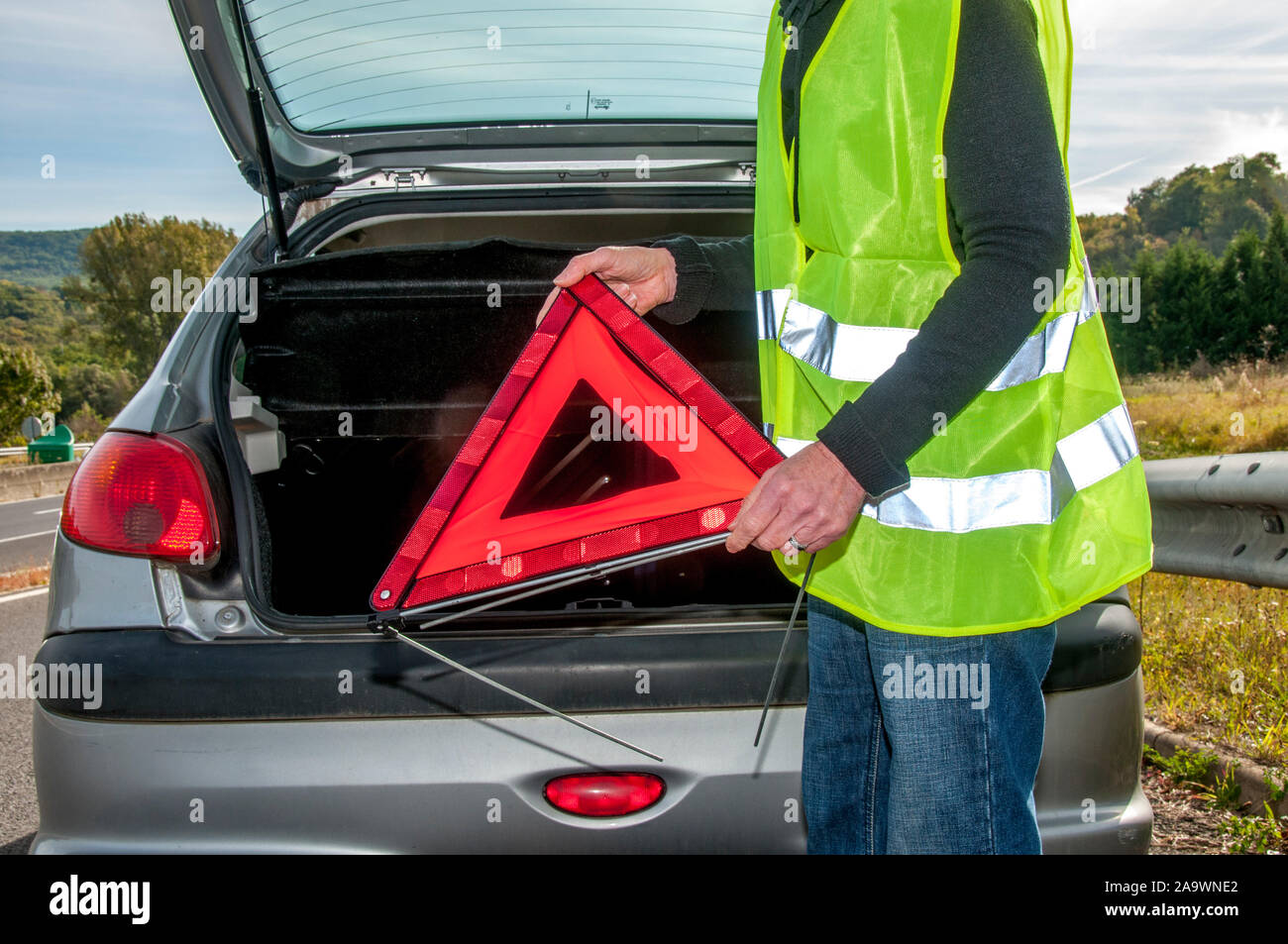 Woman getting red warning triangle out of her broken down car, France Stock Photo