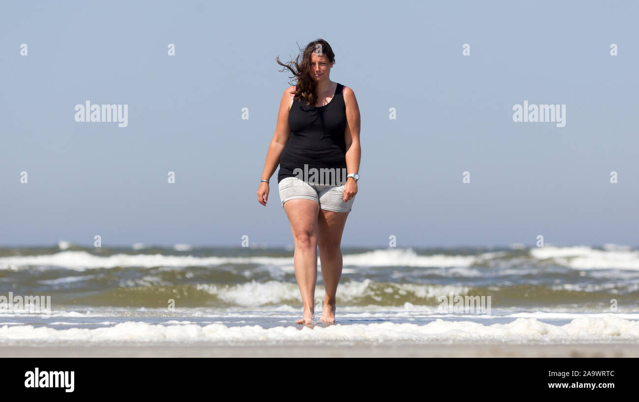 Woman is walking on the beach of a dutch isle, walking towards camera Stock Photo