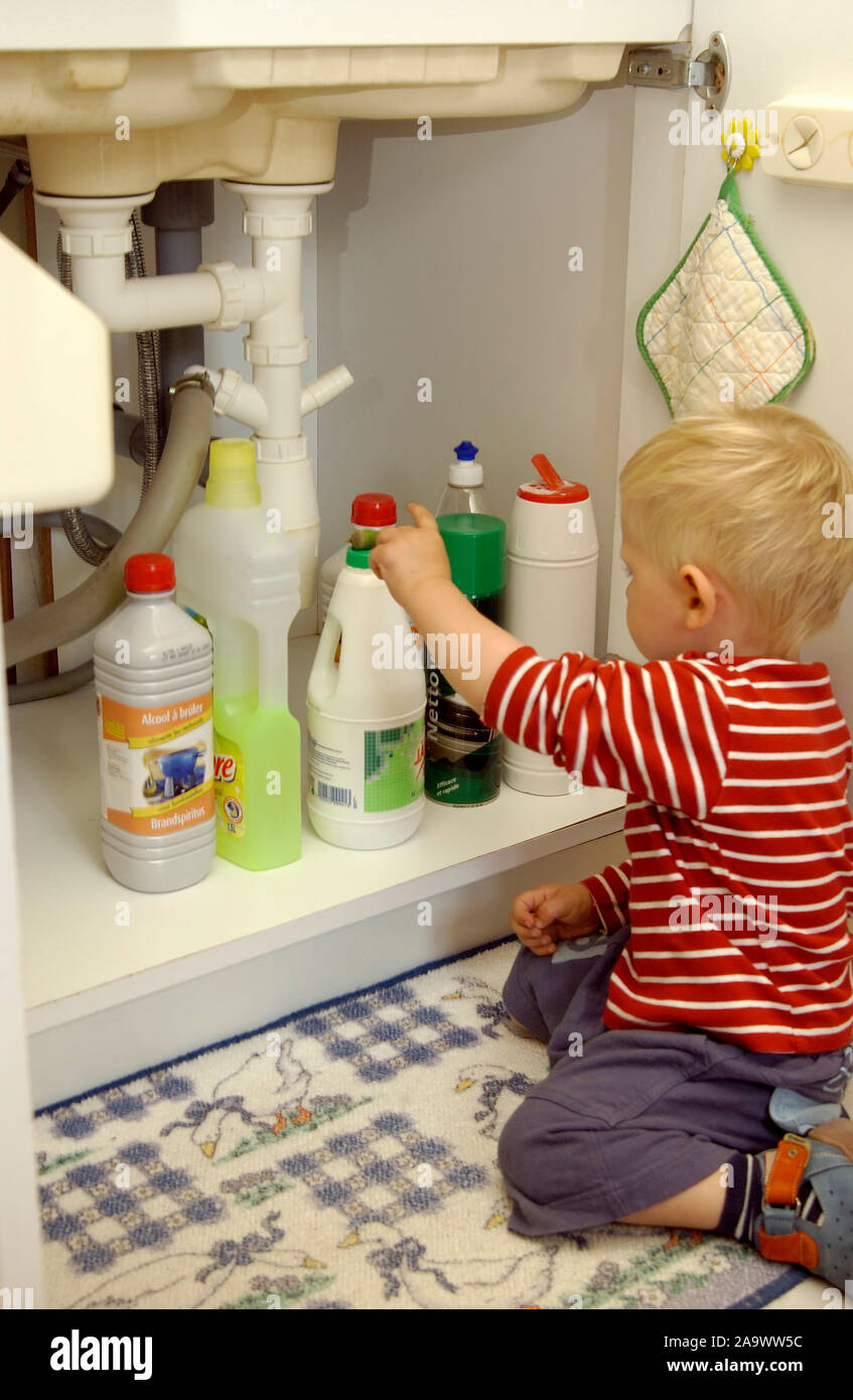 Child reaching for bottles of cleaning fluids under the sink in the kitchen, accidents concept Stock Photo