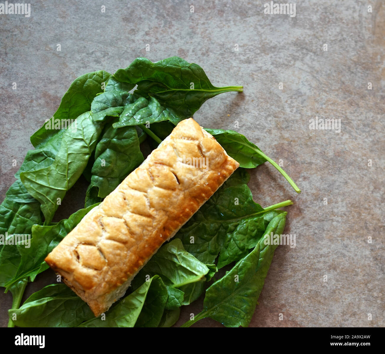 Flat lay of a sausage roll on a bed of green salad leaves on a plain brown background with white space Stock Photo