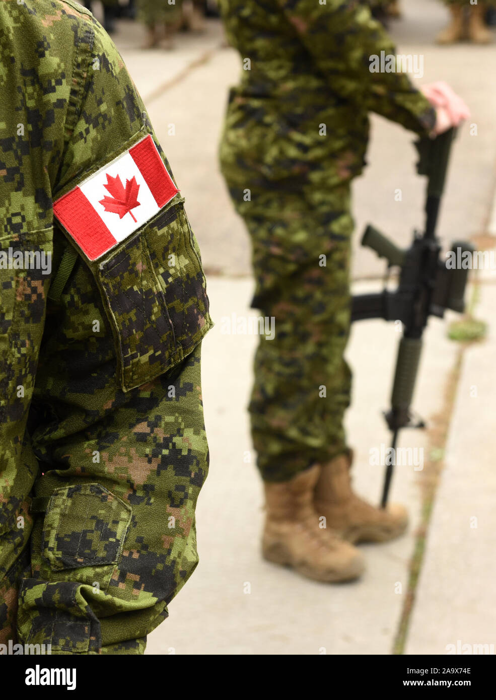 Flag of Canada on the military uniform and soldier with weapon on the background. Canadian soldiers. Canadian Army. Remembrance Day. Canada Day. Stock Photo