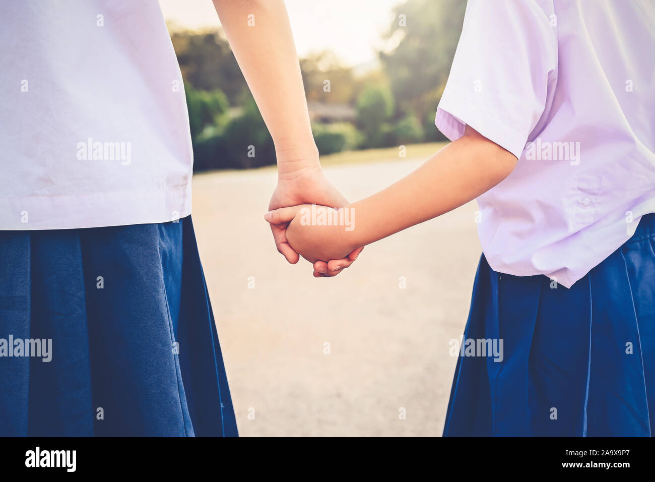 Sisters clasped holding hands waiting across the road . With hands clasped, they bind together in love friendship Stock Photo