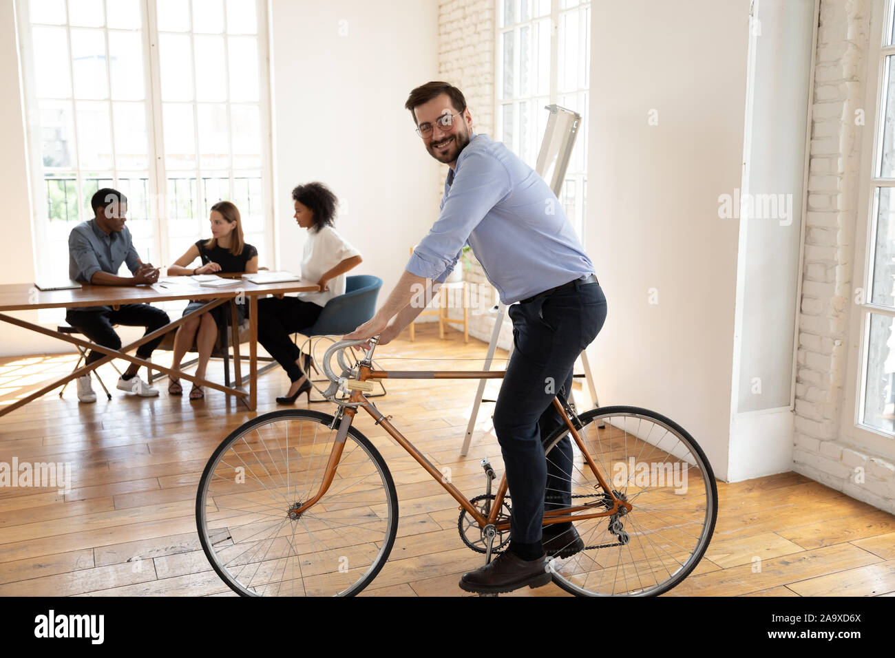 Playful happy young businessman riding bicycle at modern office. Stock Photo