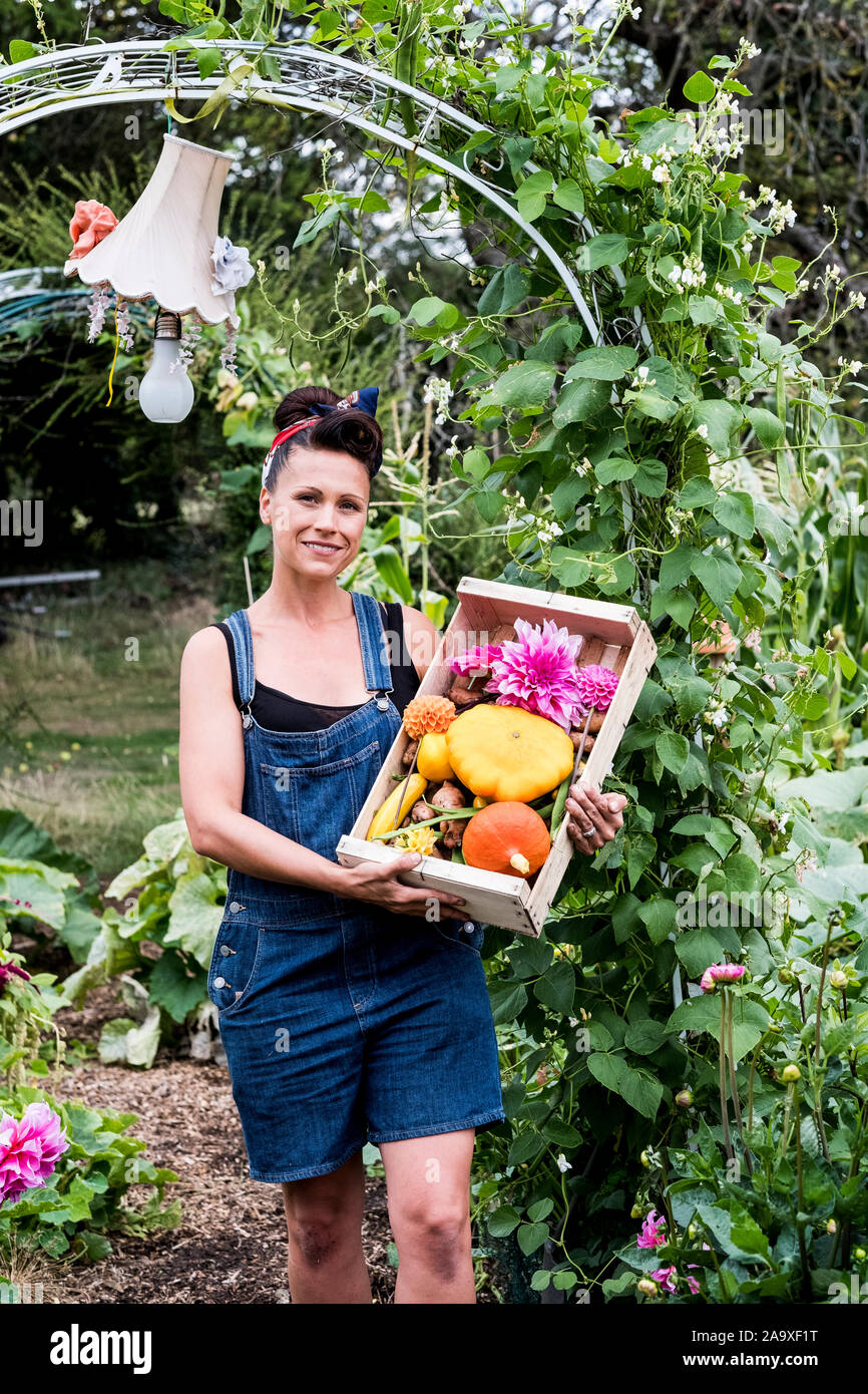 Woman standing in a garden, holding wooden crate with fresh vegetables ...