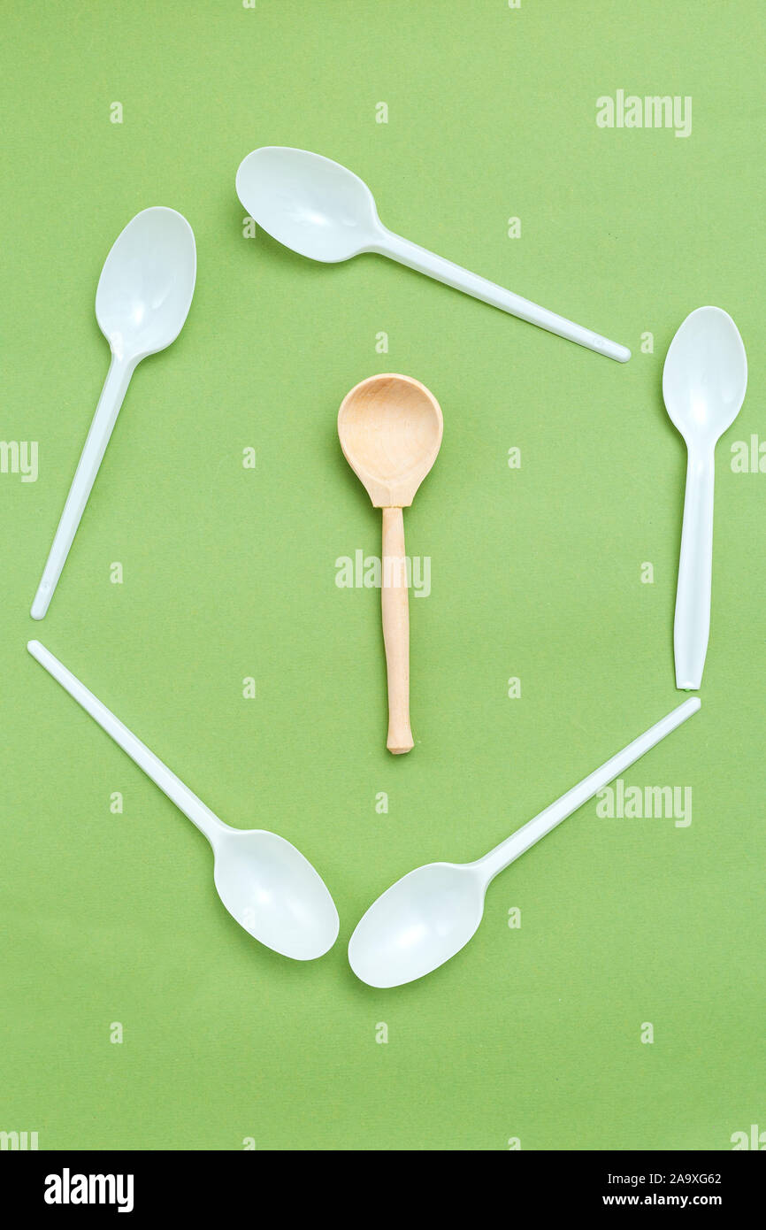 Wooden spoon with plastic alternatives on green background. Vertical