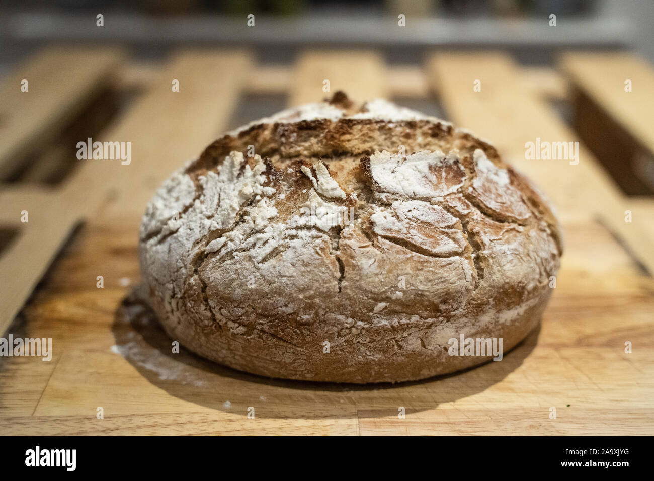 A fresh crusty rustic loaf of sourdough bread sat on a wooden bread ...