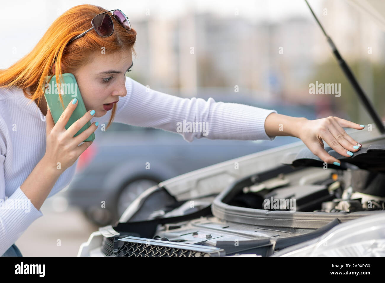 Young woman standing near broken car with popped hood talking on her ...