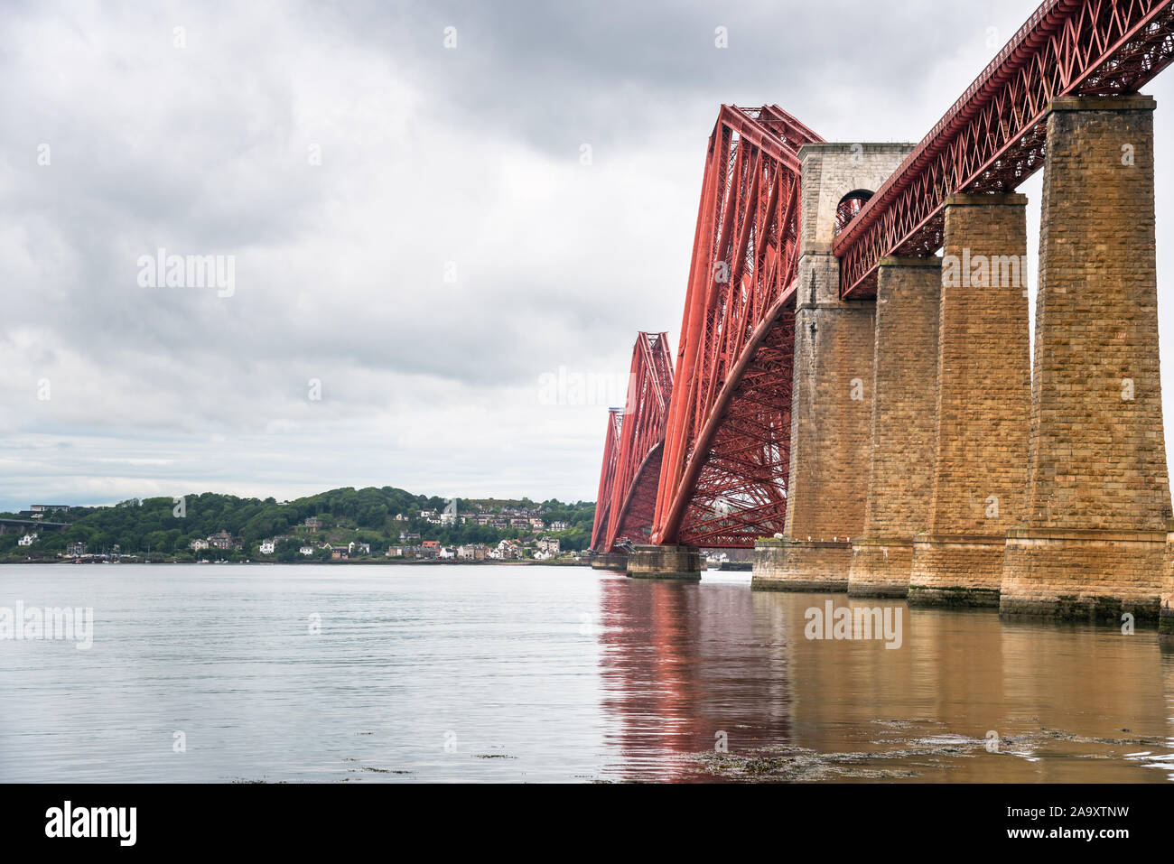 View of Firth of Forth railway bridge with the town of North Queensferry in background and cloudy sky Stock Photo