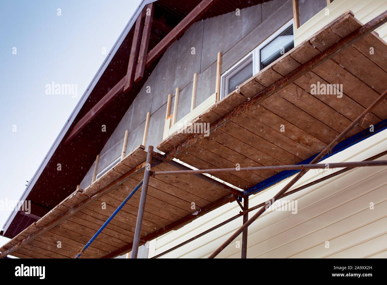 Scaffolding around house with beige siding covering walls. Construction