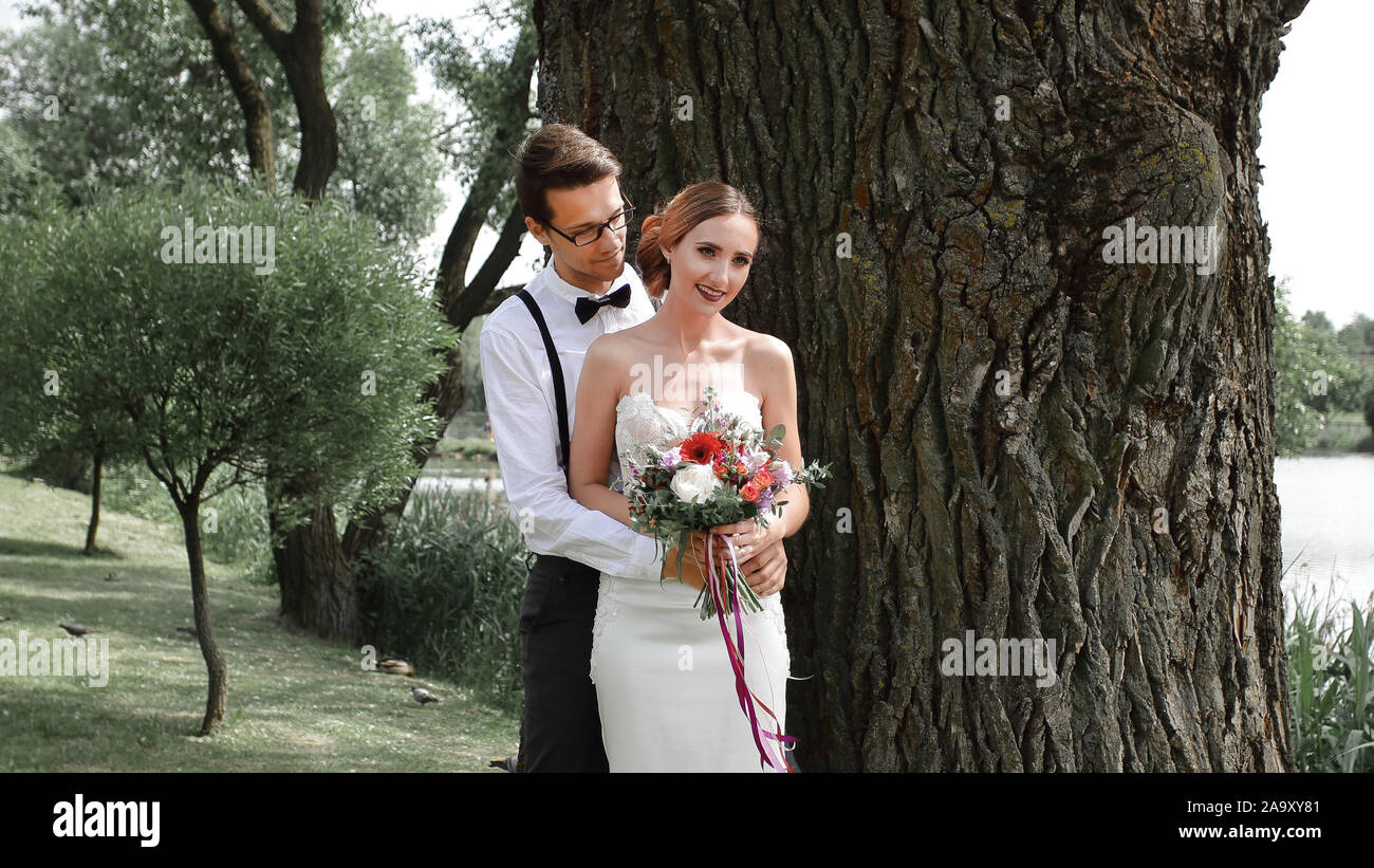 happy bride and groom standing near a big tree Stock Photo - Alamy