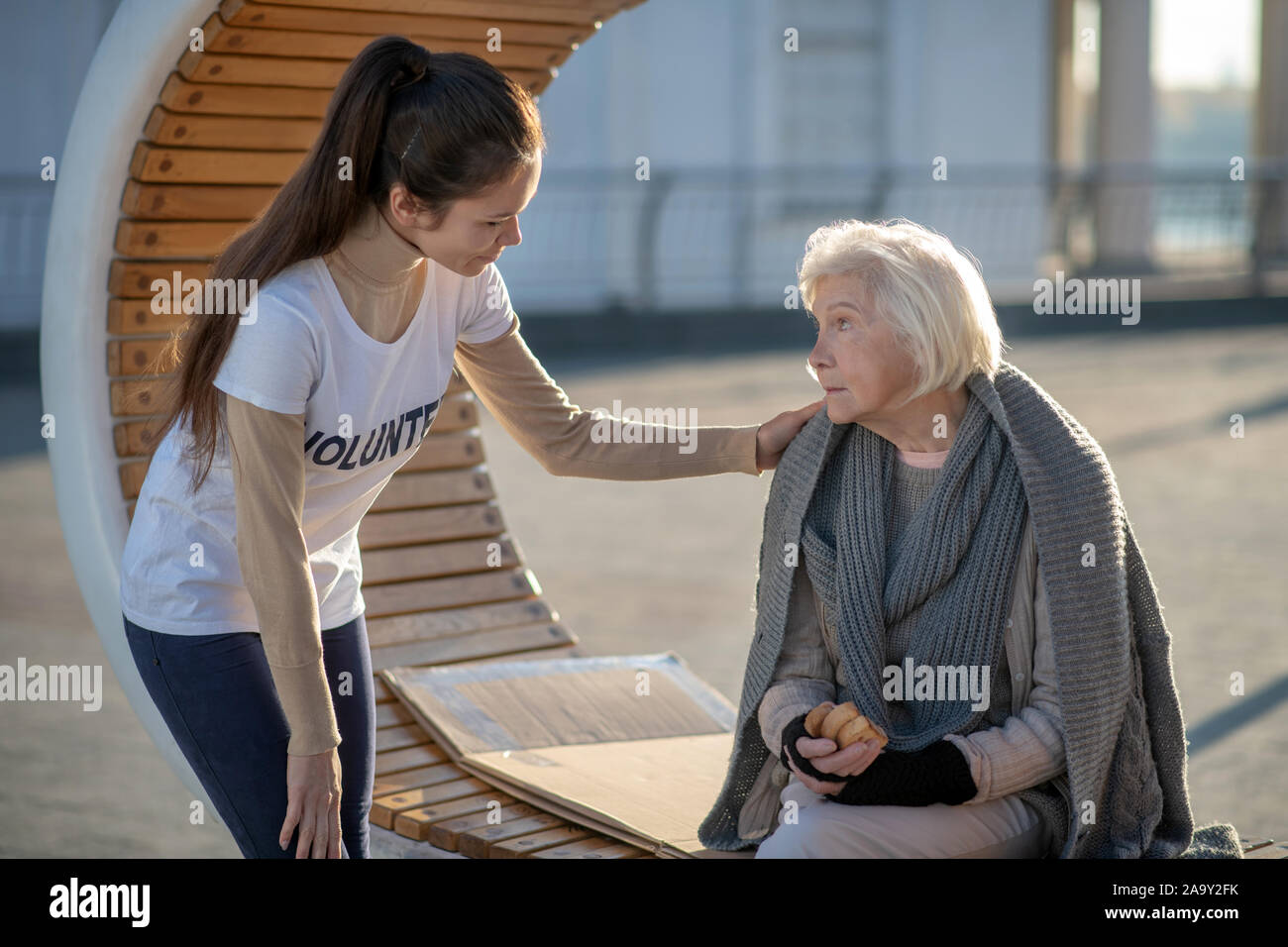 Kind-hearted young volunteer coming to poor homeless woman Stock Photo