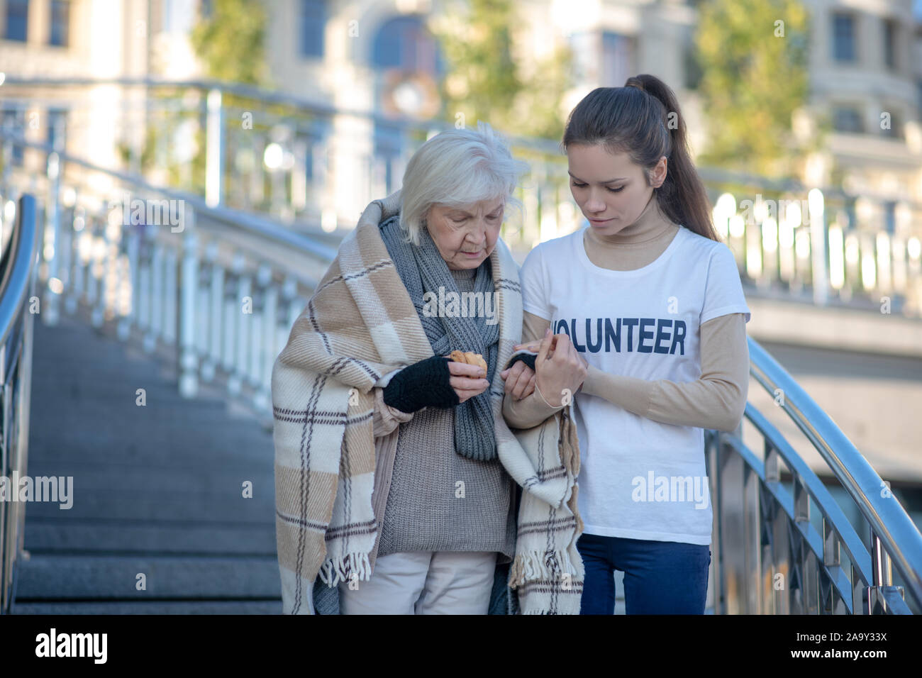 Young kind volunteer helping homeless woman to walk Stock Photo