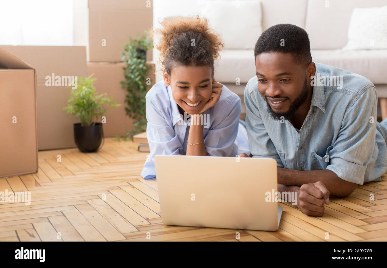 Black Spouses Using Laptop Lying On Floor Indoor Stock Photo