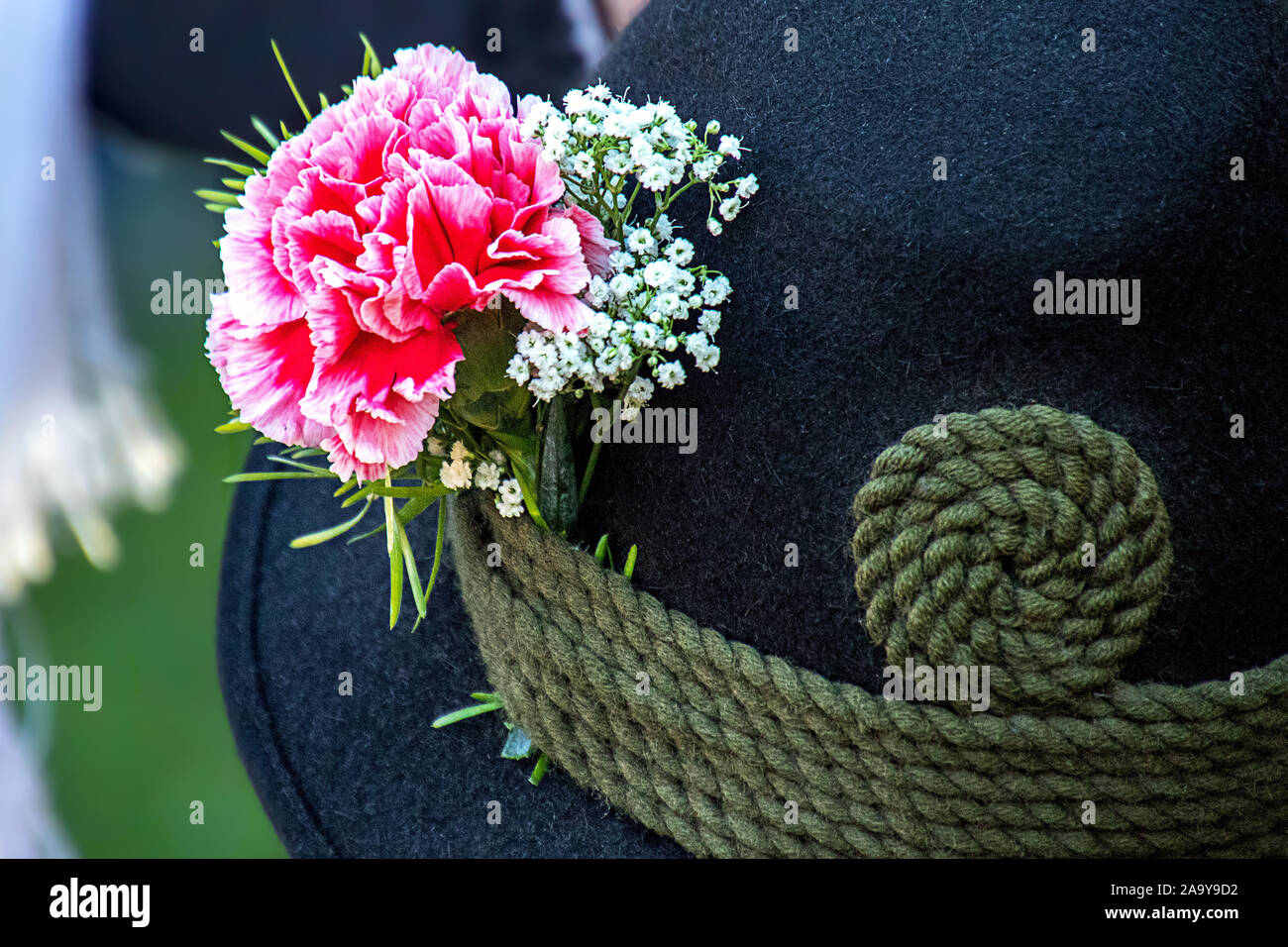 close up of a black  hat made of loden with carnation and gypsophila and a green cord Stock Photo