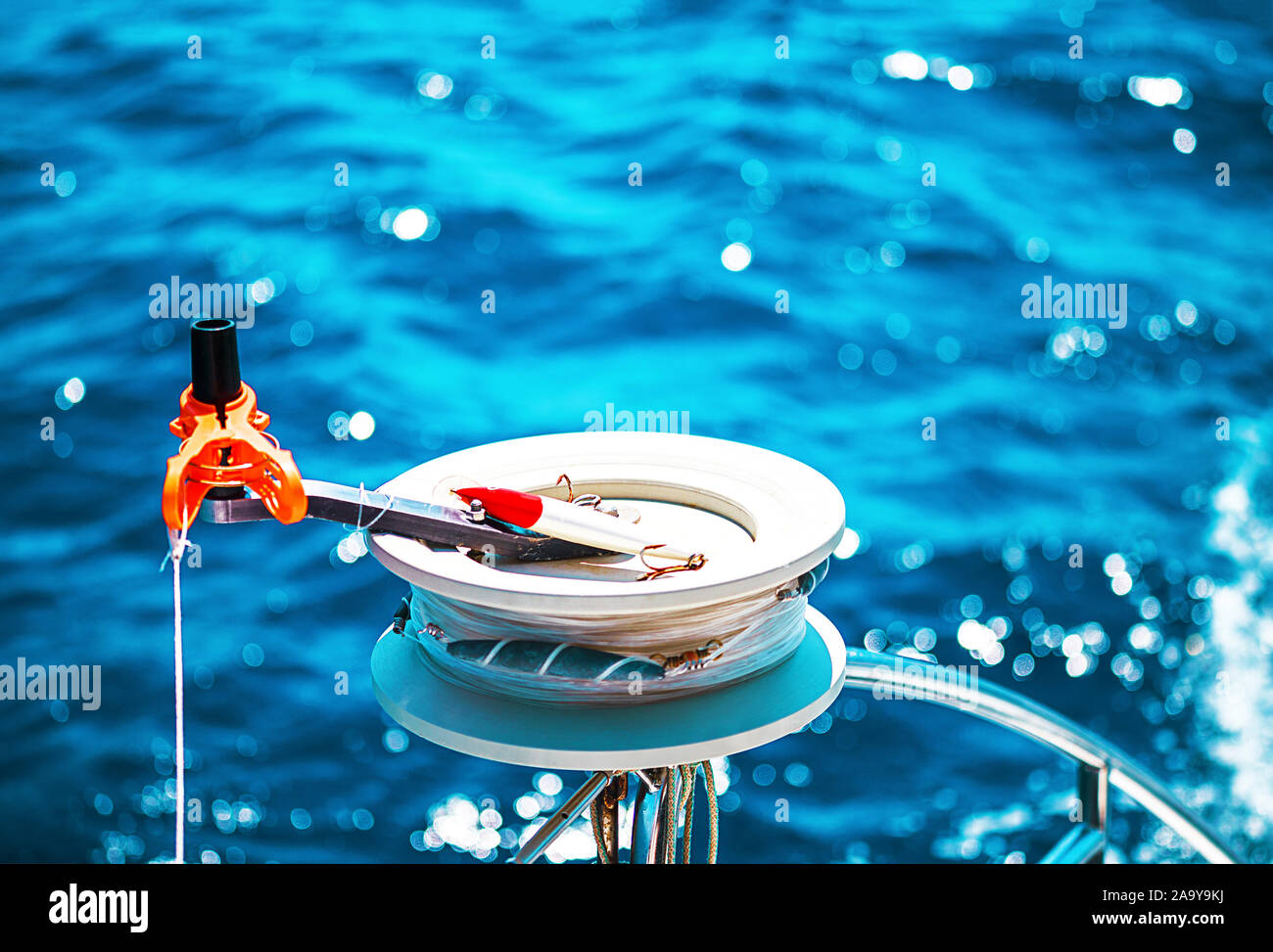 Fishing reel or rod reel, rod. Sailing yacht catamaran in the sea in Greece, turquoise waters of Aegean Sea near Athens. Famous travel sailing destination in Europe. Sailboat. Selective focuse. Stock Photo